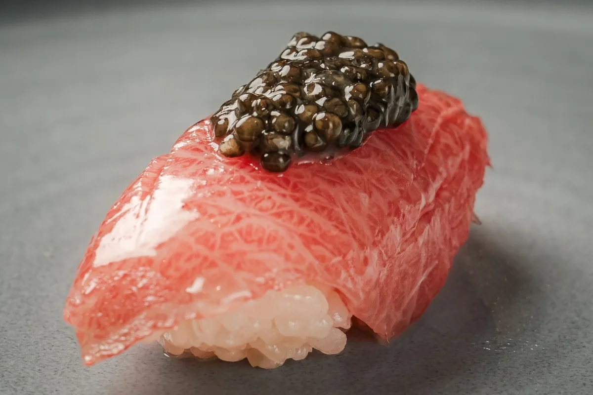 A piece of tuna nigiri topped with a spoonful of dark caviar
