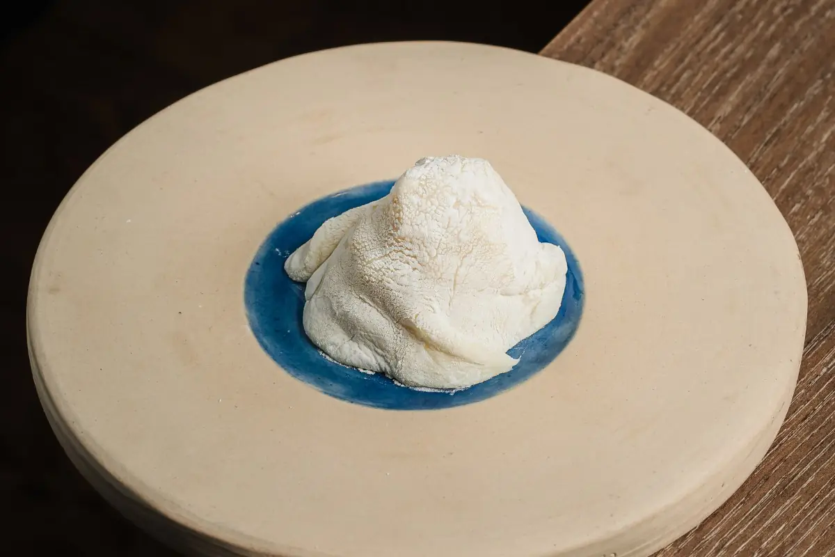 Draped white dish resembling cream or dough on a ceramic plate with a blue-glazed center