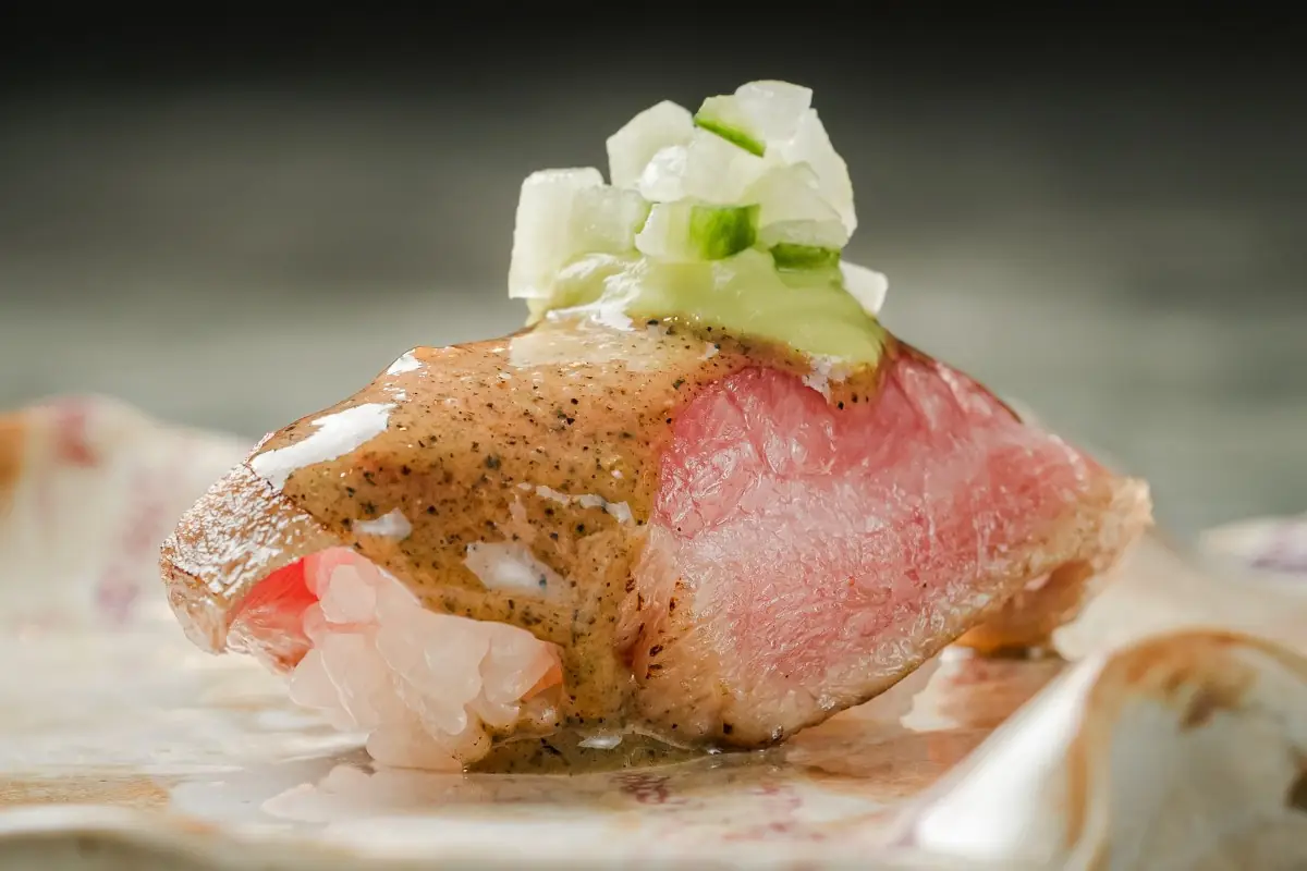 Close-up of a nigiri sushi topped with sauce and diced cucumber