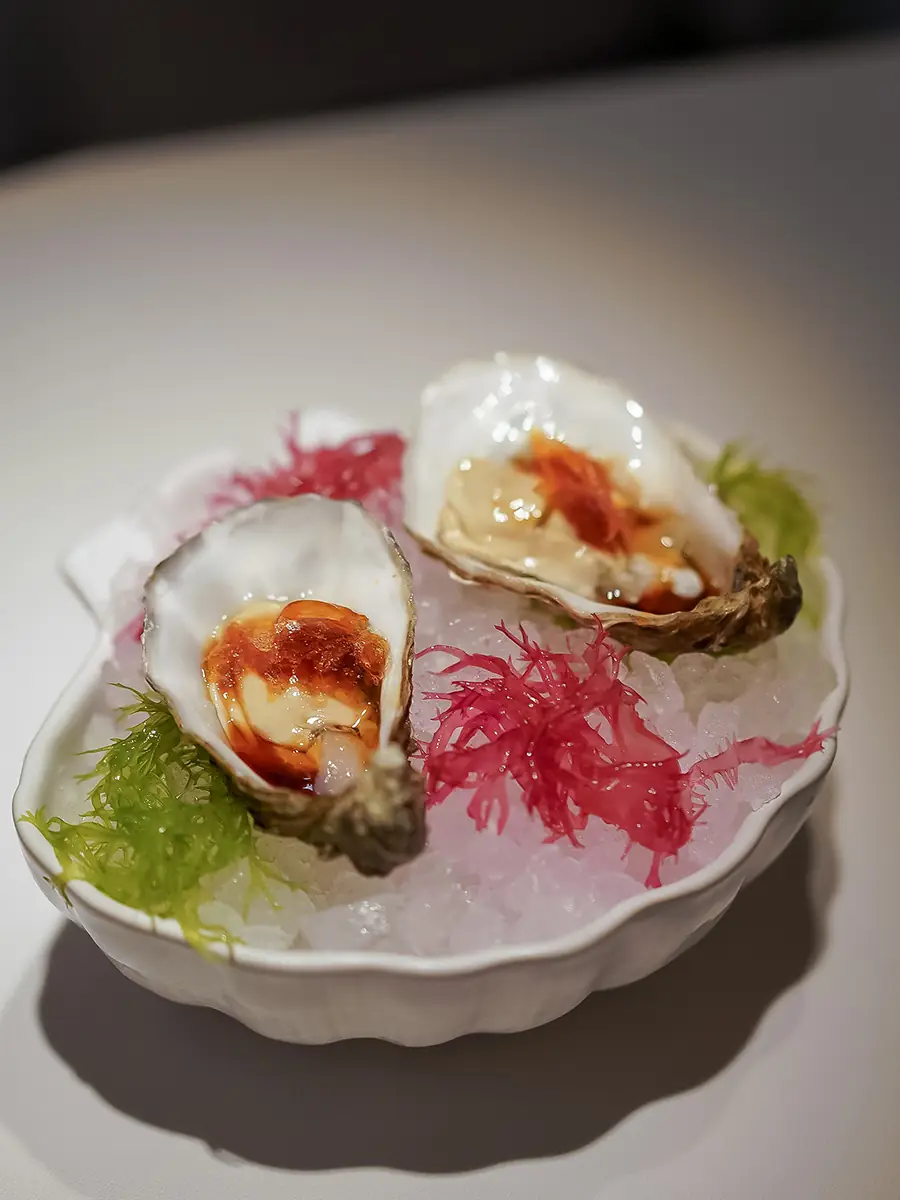 Two oysters on ice topped with a spiced sauce, garnished with seaweed