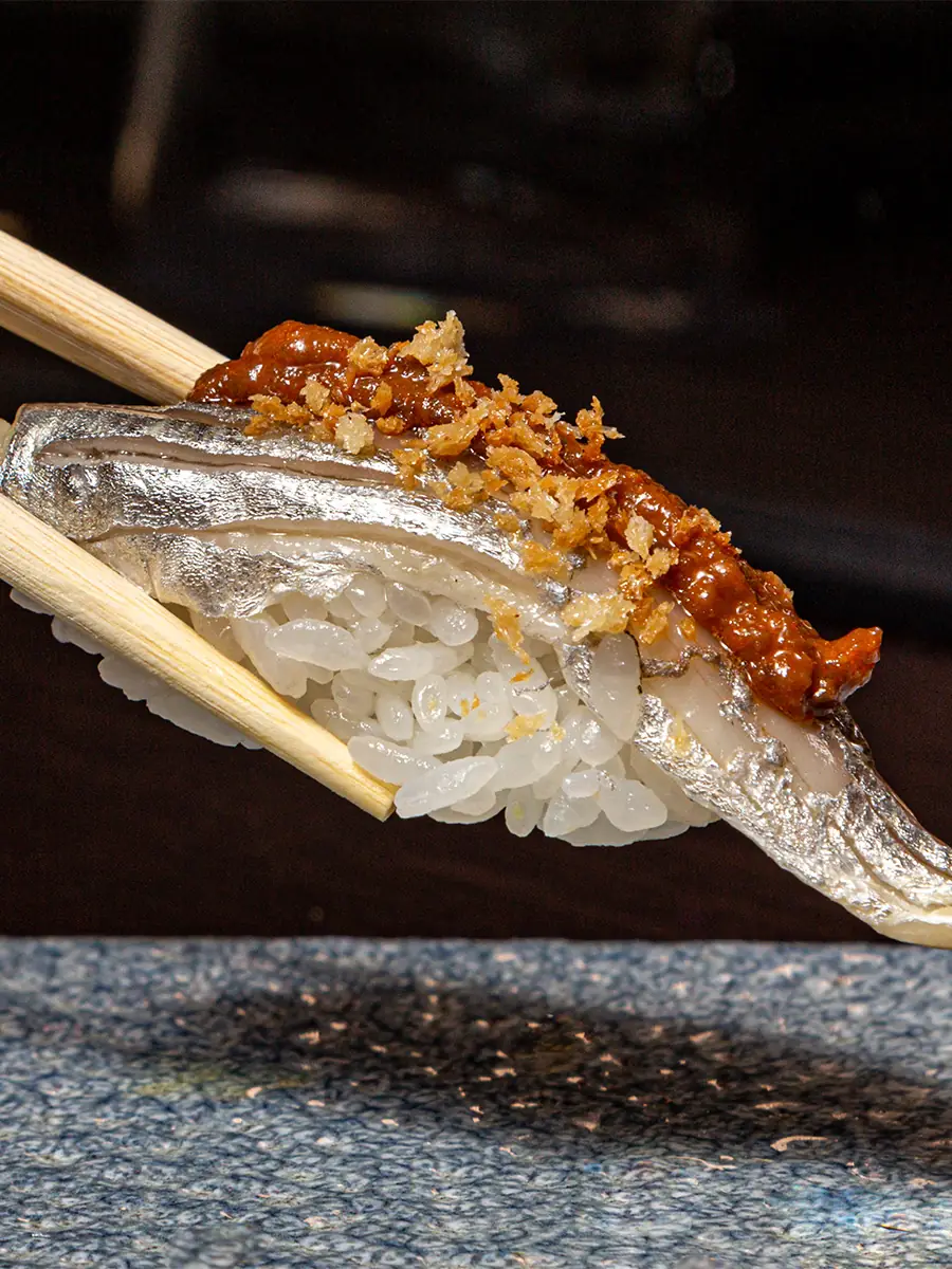 Nigiri sushi topped with spicy sauce and crispy shallot, held with chopsticks