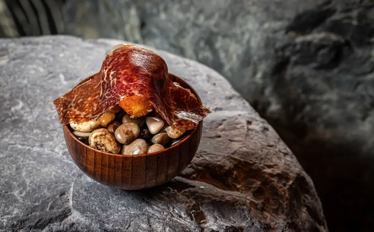 A roasted dish garnished with herbs, served in a small bowl atop a dark stone slab.