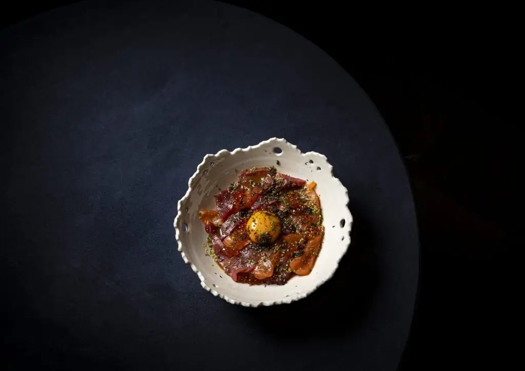 Tuna tartare with egg yolk in a ceramic bowl on a dark table