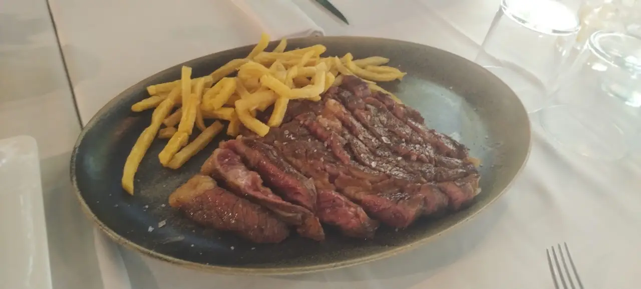 Sliced grilled steak with a side of french fries on a dark plate.