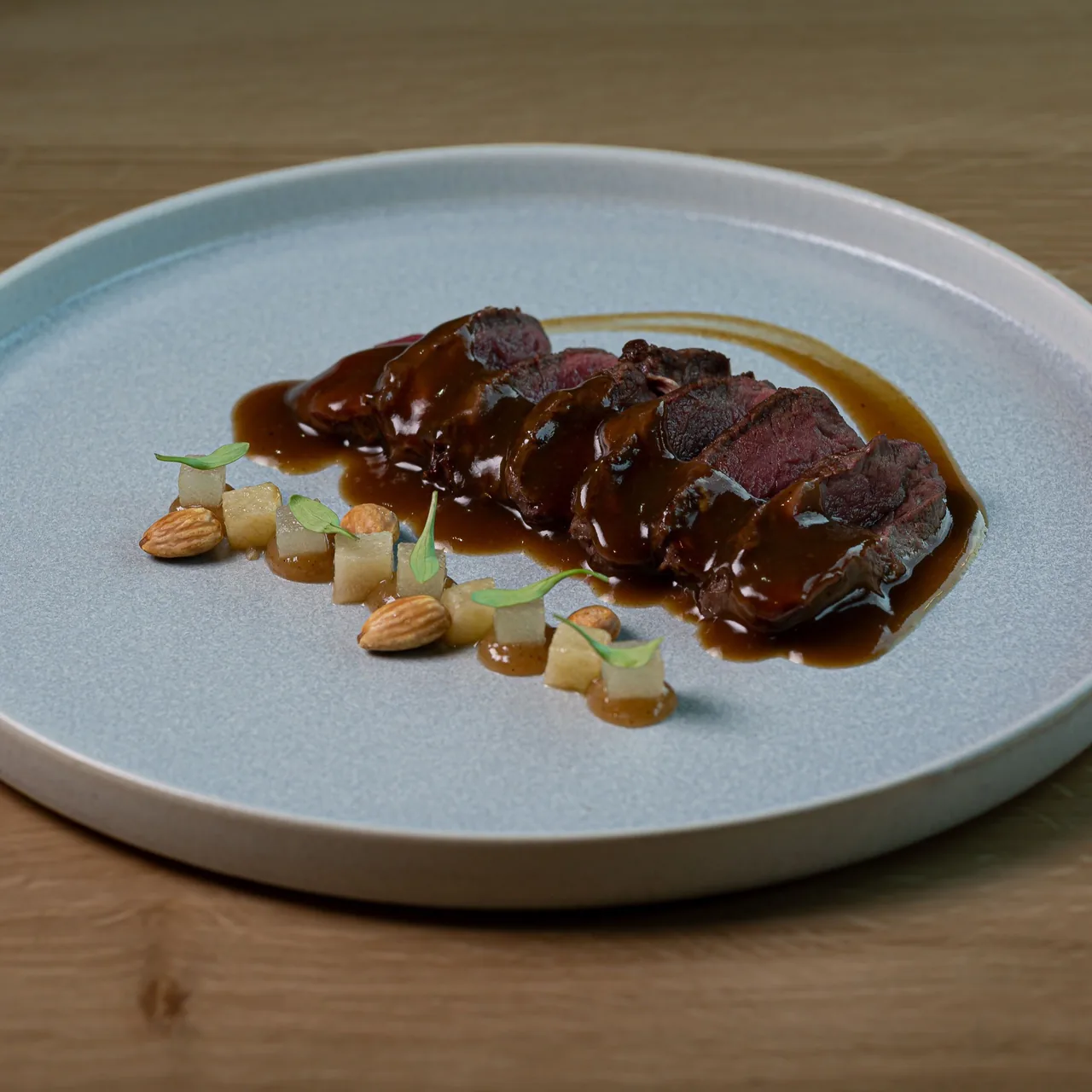 A round grey plate of sliced dark meat in sauce with almonds and pear pieces