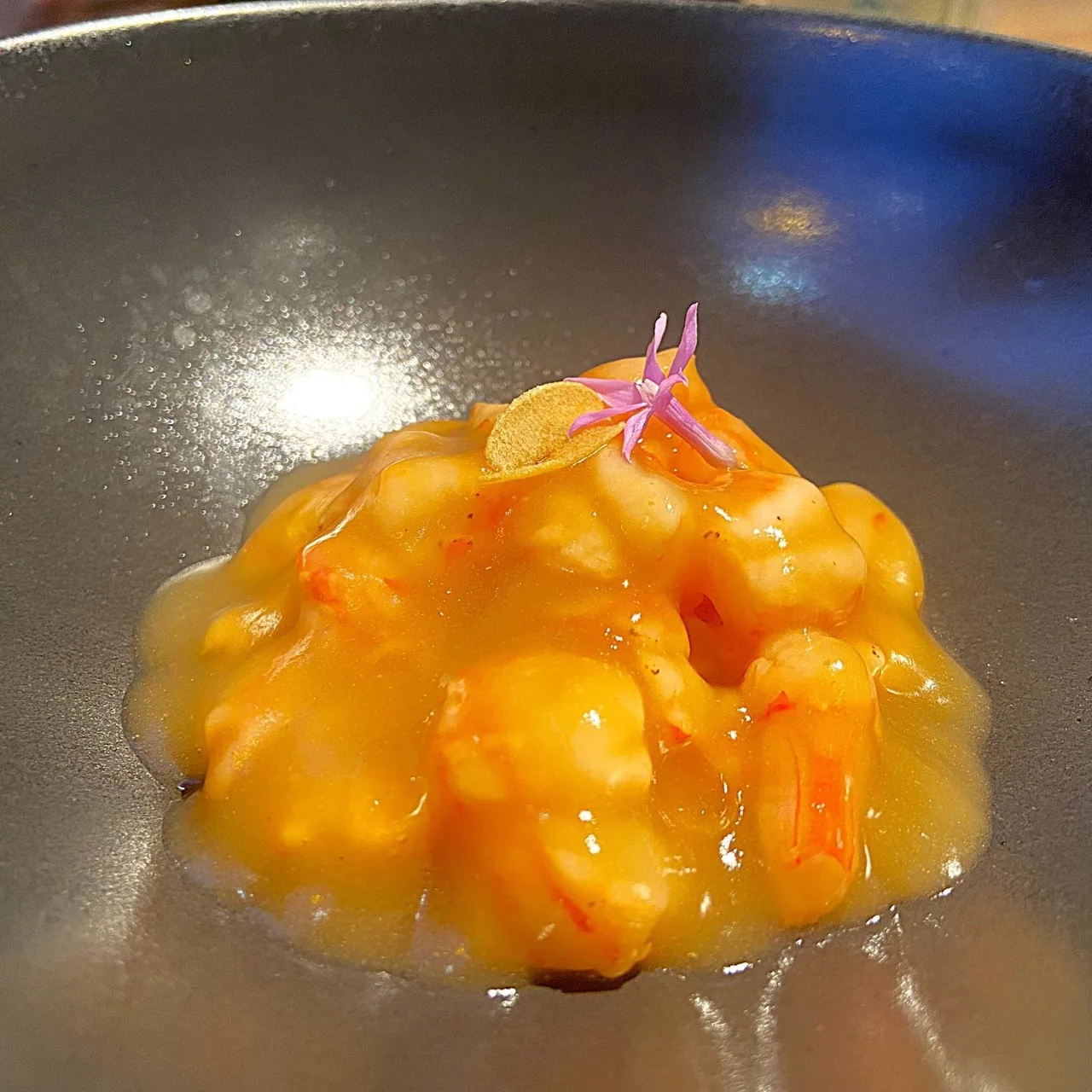 A mound of bright orange creamy seafood dish garnished with a small flower