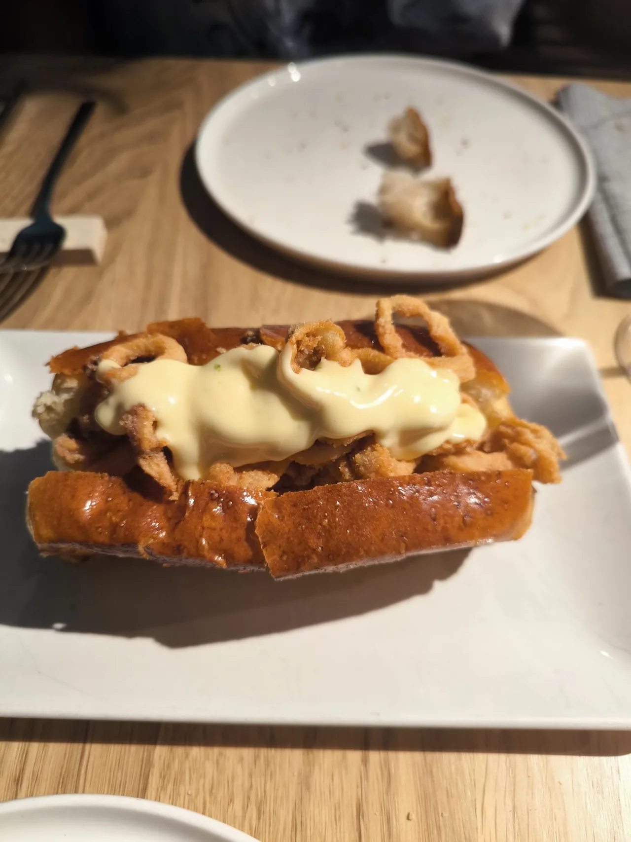 A toasted brioche roll filled with fried squid and topped with a pale citrus aioli on a white plate
