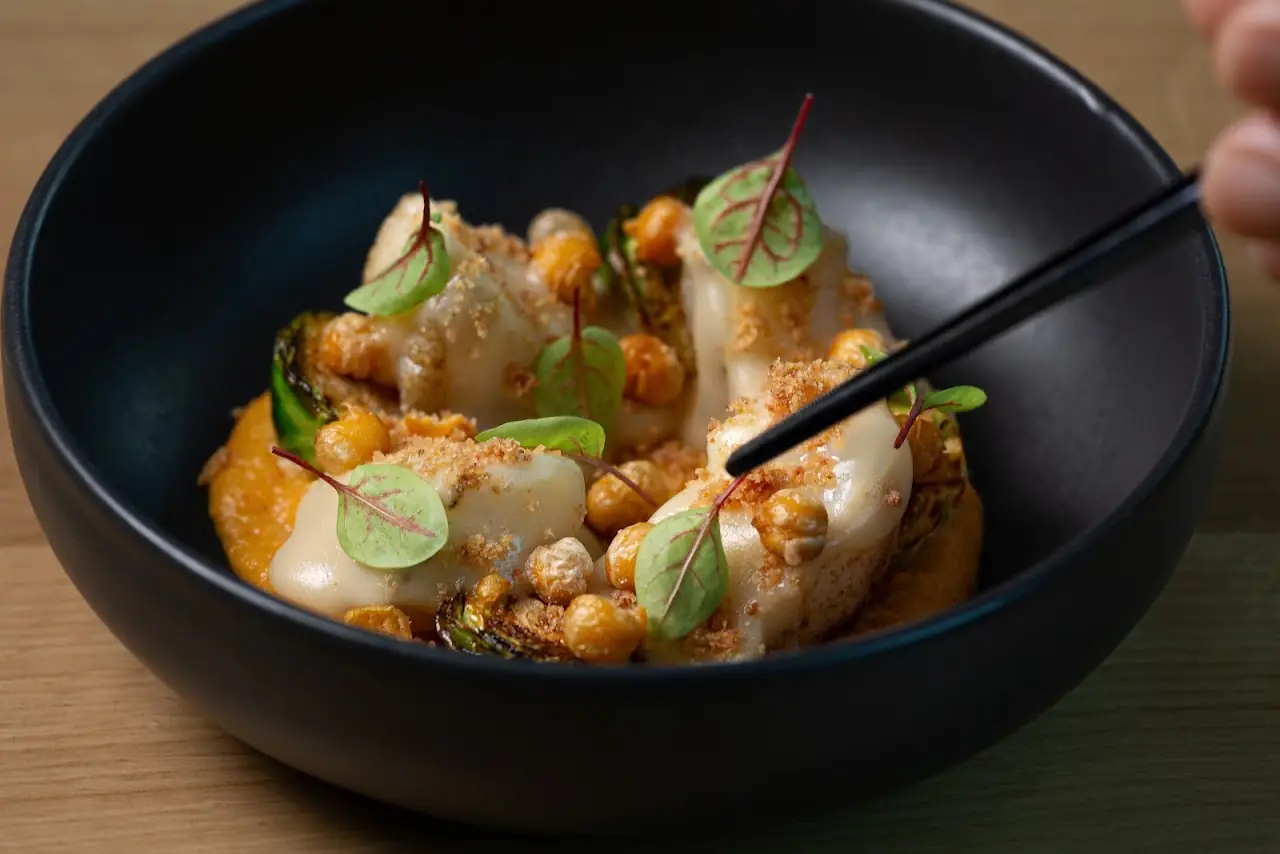 Scallops with corn kernels and herbs in a dark bowl, chopsticks resting on the dish.