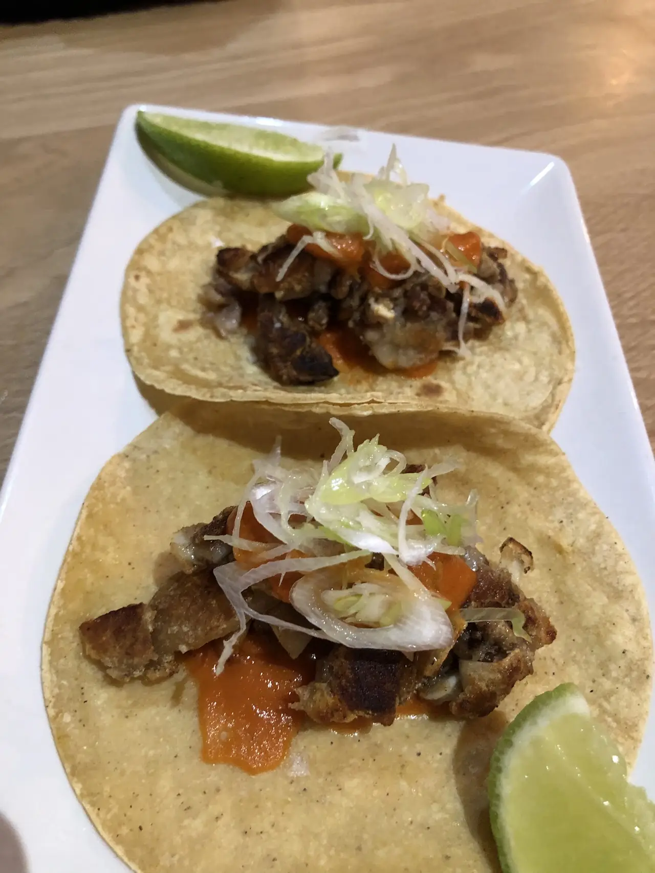 Two tacos with grilled meat, pickled onion and lime wedges on a plate.