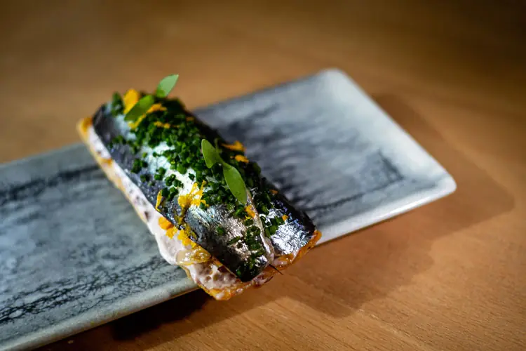 Plated fish fillet dish garnished with chives and herbs on a rectangular plate
