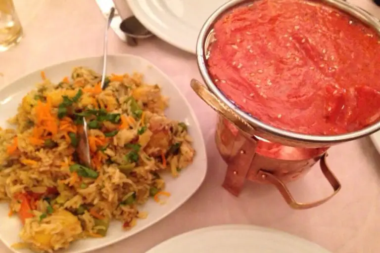 Plate of vegetable biryani rice with a copper serving pot of red curry
