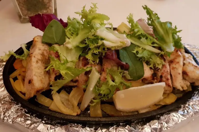 Sizzler plate of grilled chicken tikka strips topped with mixed salad leaves and a lemon wedge