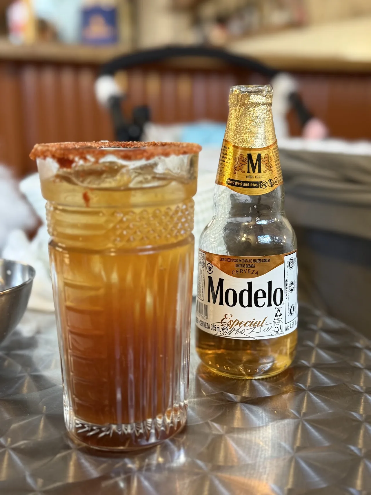 A cocktail in a salt-rimmed glass beside a bottle of Modelo beer