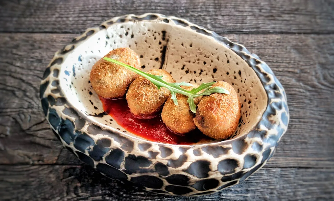 A ceramic dish of croquettes in red sauce garnished with herbs