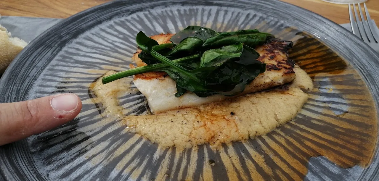 A piece of fish with greens plated over a creamy sauce
