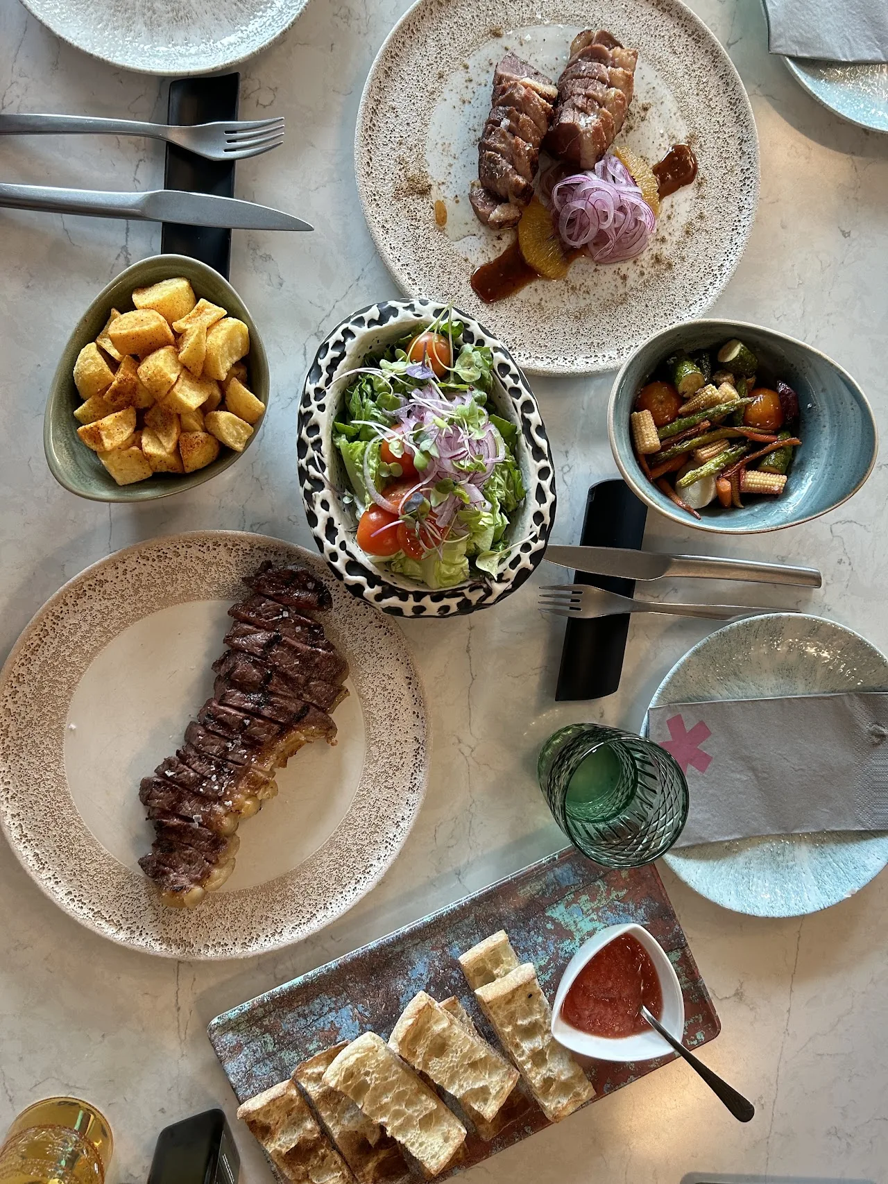 An overhead spread of steak, roasted potatoes, salad, and croquettes