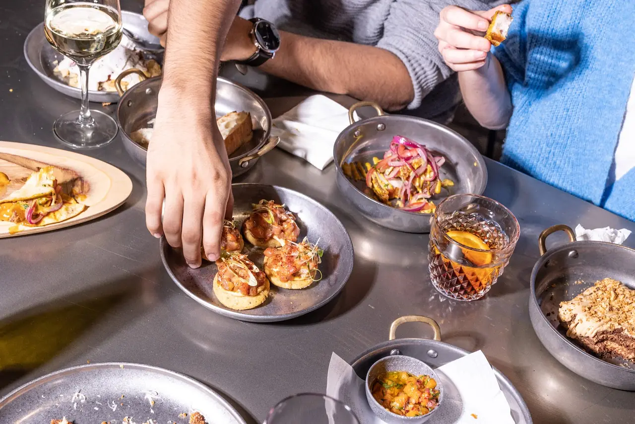 Table spread of small plates: tostada with tuna tartare, tacos, cocktail with orange slice, white wine