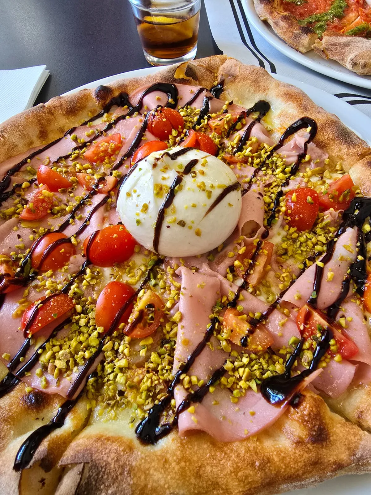 A pizza topped with burrata, prosciutto, cherry tomatoes, and a balsamic drizzle