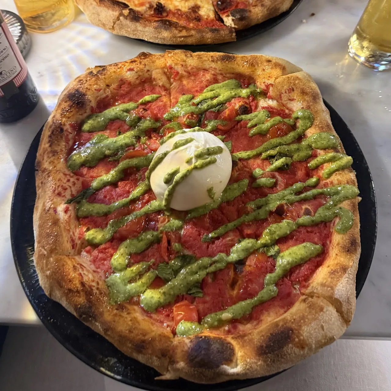A pizza topped with burrata and a green pesto drizzle