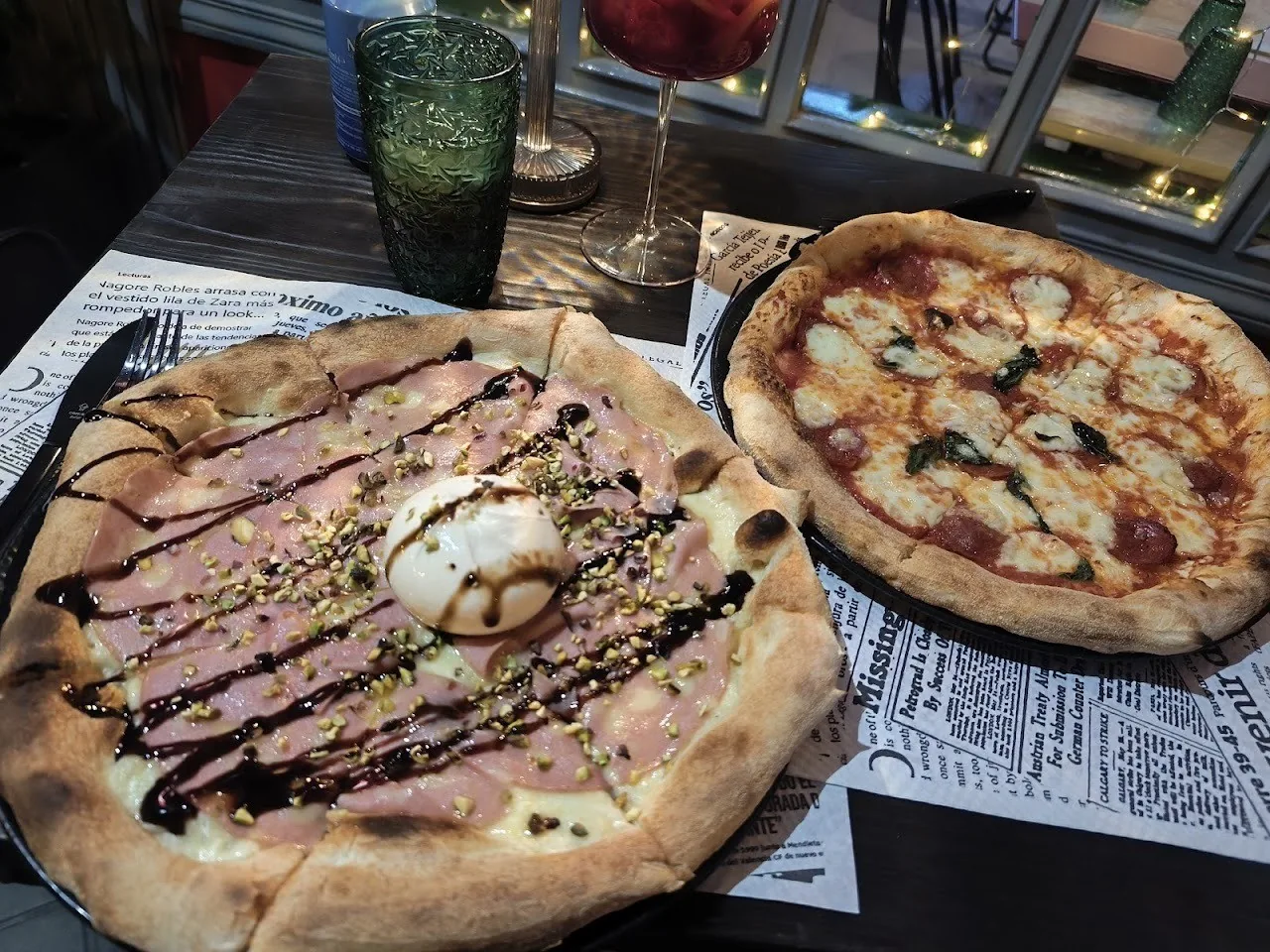 Two pizzas on a table, one topped with ham and a ball of white cheese and one with tomato and mozzarella