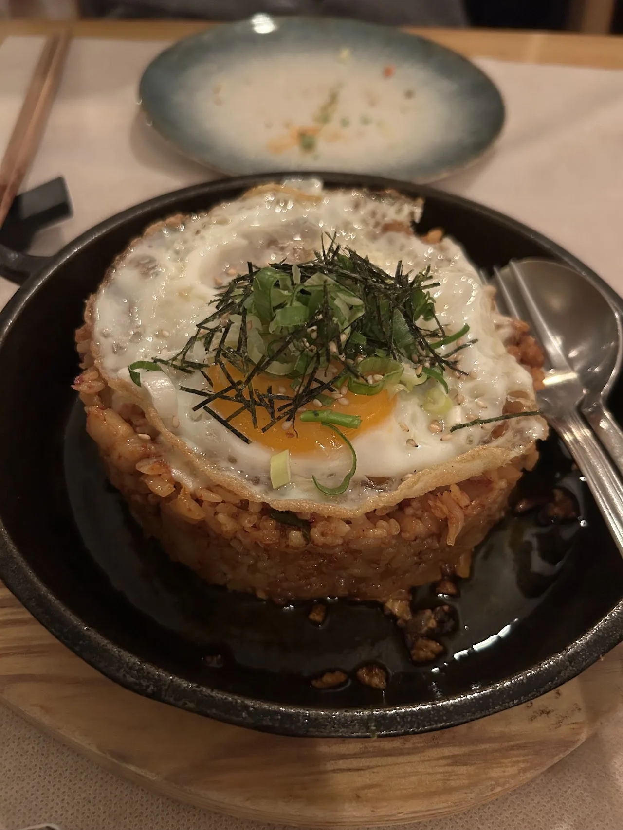 A stone bowl of fried rice topped with a sunny-side-up egg and scallions