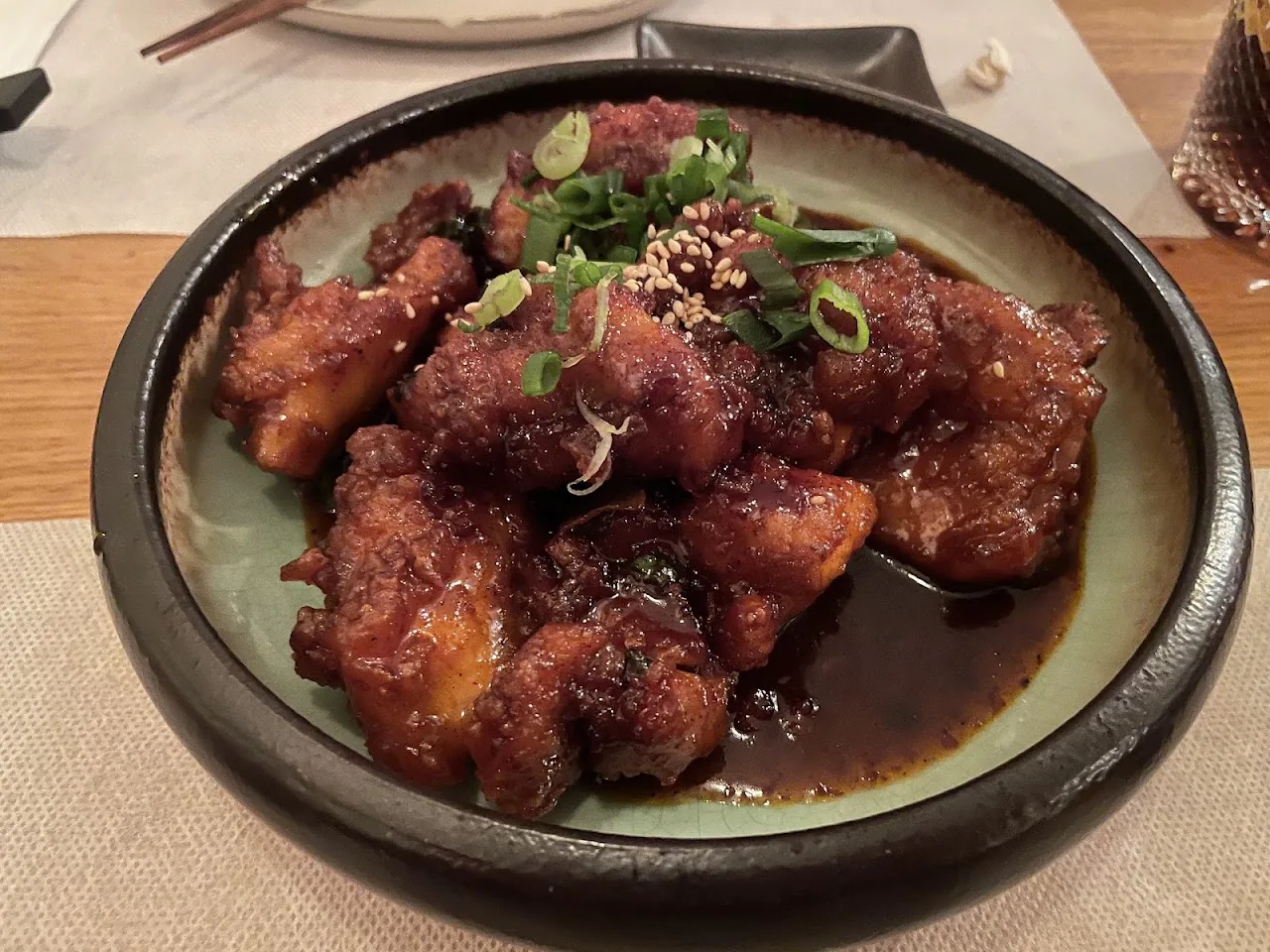 A plate of glazed fried chicken pieces topped with scallions and sesame seeds
