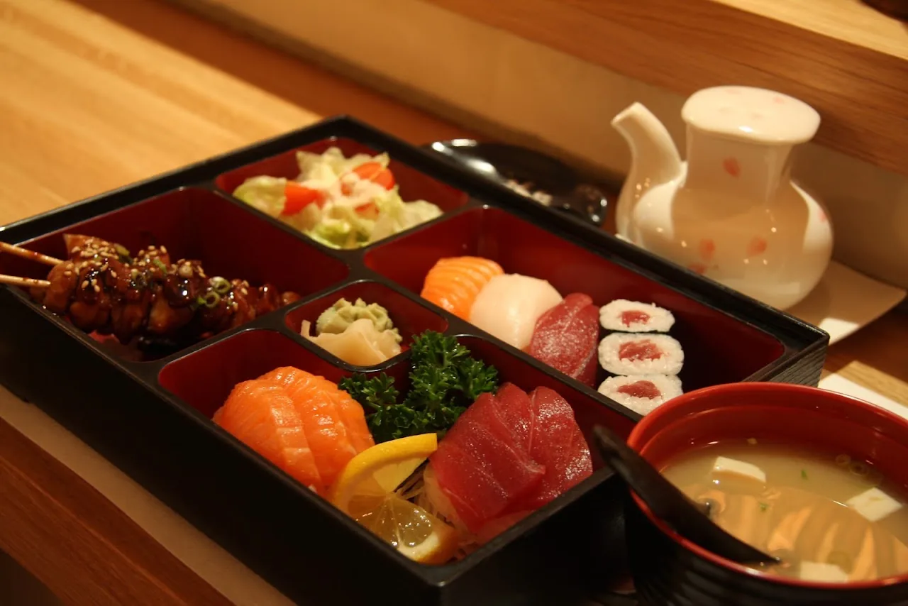 A bento box with sashimi, sushi rolls, tempura, and a small bowl of miso soup