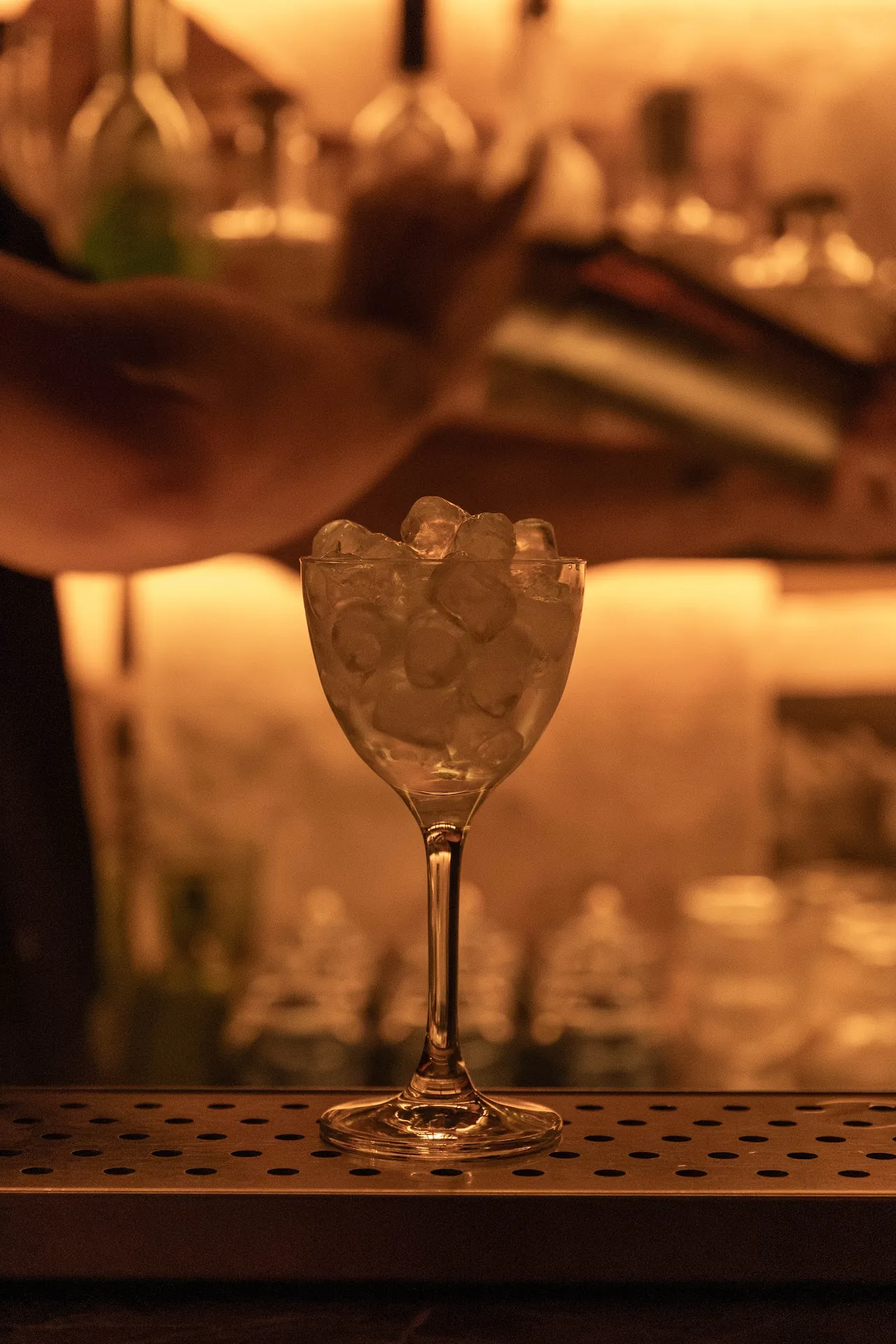 A cocktail glass filled with ice being prepared behind a cocktail shaker