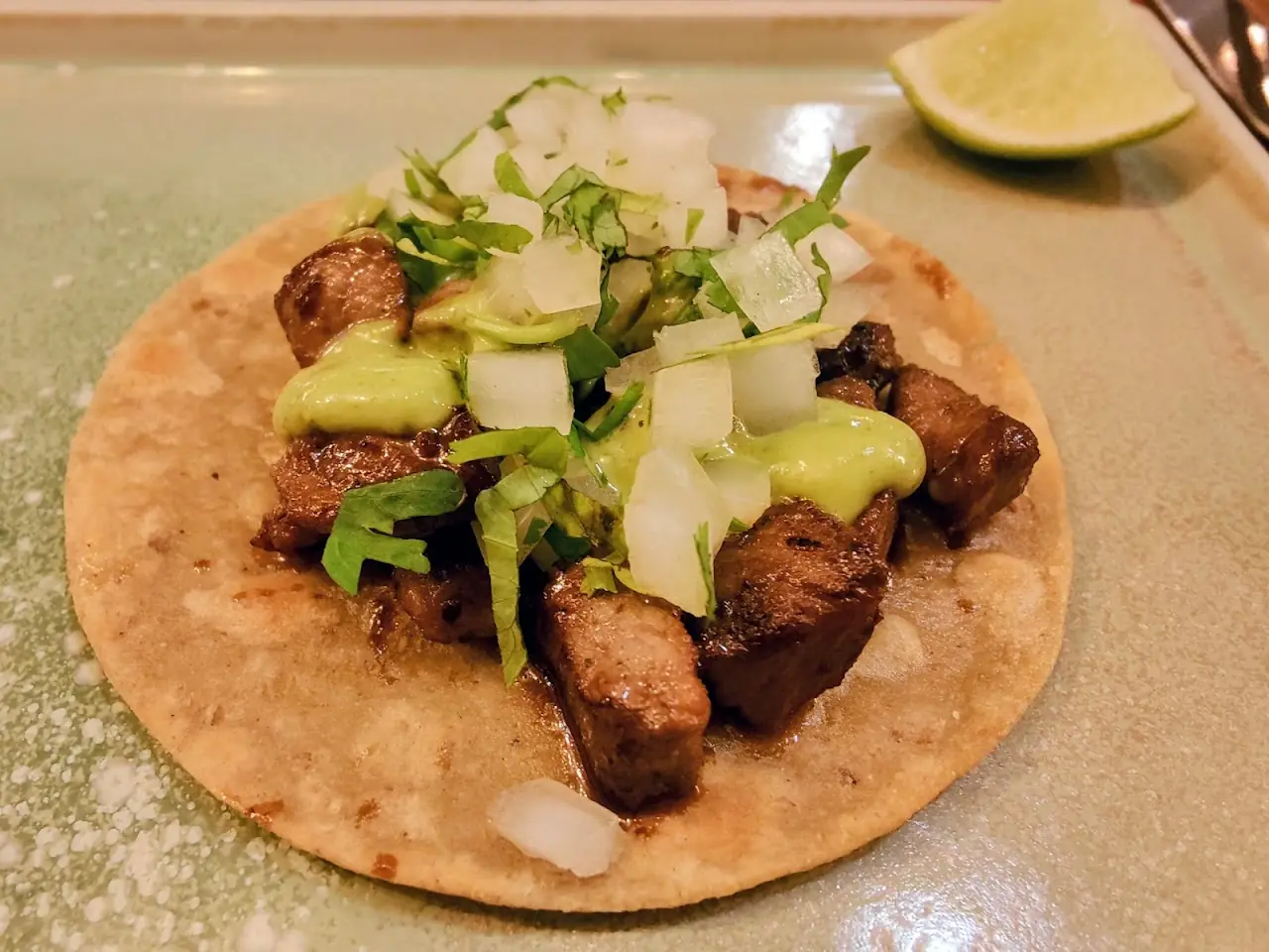 Taco topped with grilled meat, shredded cabbage, and cheese.