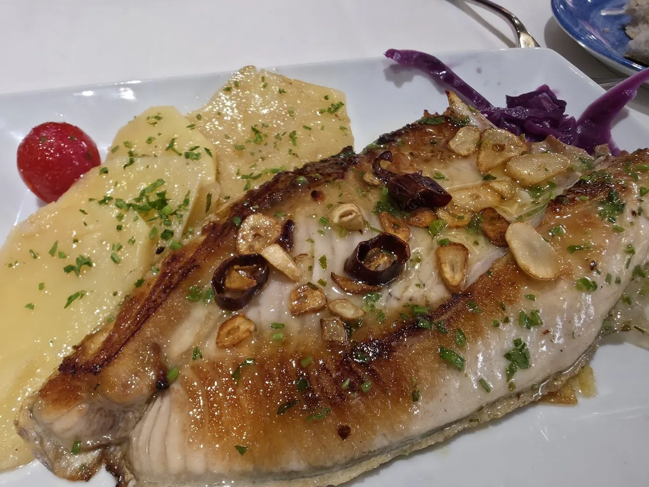 A fillet of fish with sliced garlic in a pale sauce on a plate