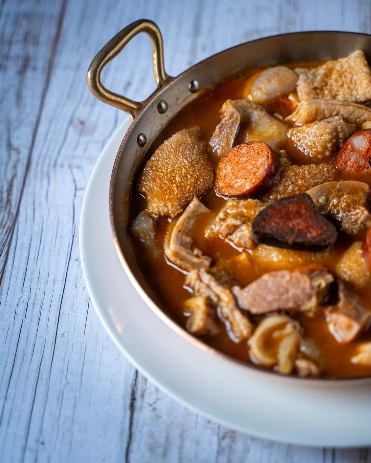 A copper pan of stew with pieces of tripe and sausage in an orange sauce