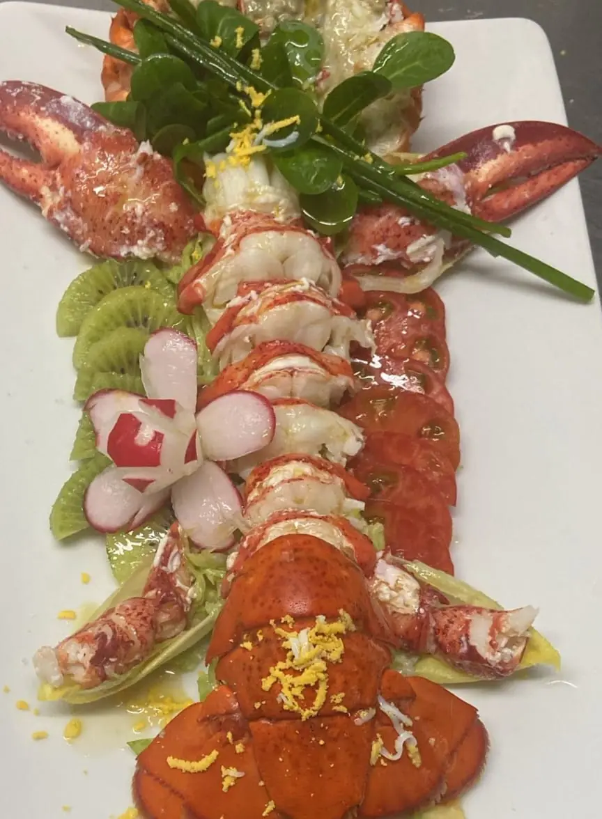 Whole lobster sliced and arranged with kiwi, radish, tomato and greens on a white platter