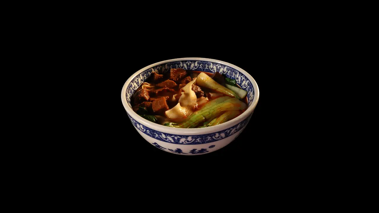 Blue-and-white patterned bowl of Lanzhou hand-pulled noodle soup with braised beef chunks, wide flat noodles, and bok choy in a spiced broth, Jin Da Le