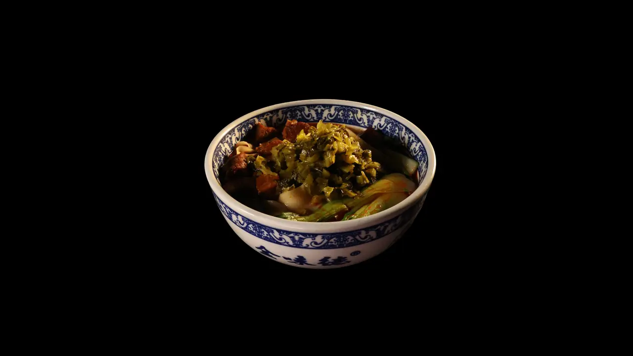 Blue-and-white patterned bowl of noodle soup topped with chopped pickled mustard greens, braised meat cubes, and bok choy, Jin Da Le