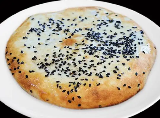 Round sesame-topped baked flatbread (shaobing) sprinkled with black sesame seeds on a white plate
