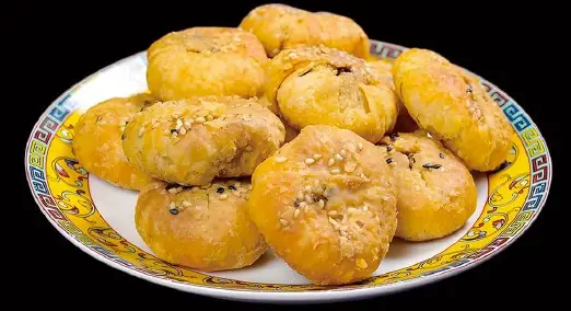Pile of golden sesame-flecked baked pastry buns on a Chinese-patterned rimmed plate