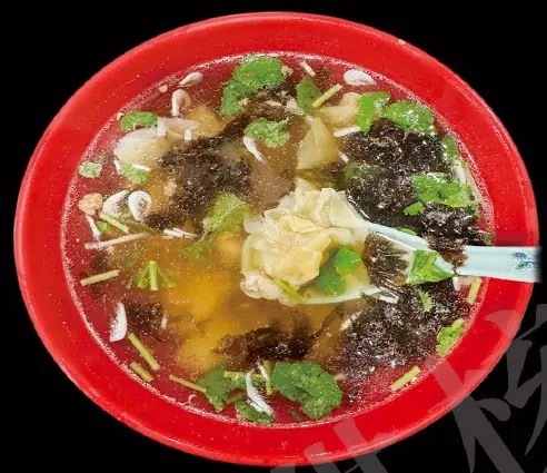 Wonton soup with seaweed, cilantro and a dumpling lifted on a spoon in a red bowl