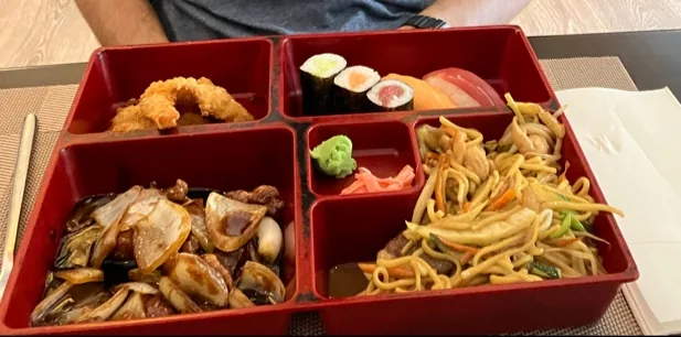 A bento box with tempura, sushi, noodles, and other dishes