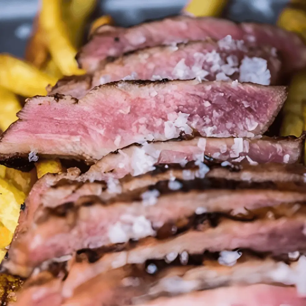 Close-up of sliced medium-rare grilled steak topped with flaked sea salt, fries alongside