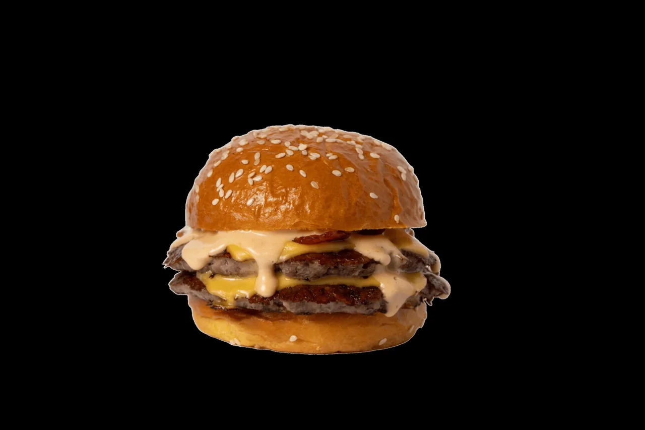 A double burger with sesame bun, cheese and sauce against a black background