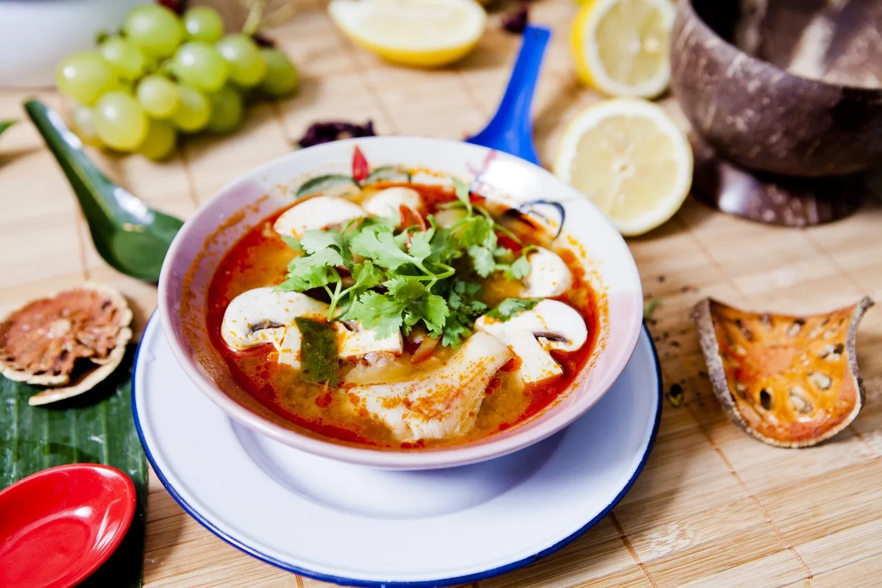 A bowl of red soup with mushrooms and fresh coriander on a bamboo mat