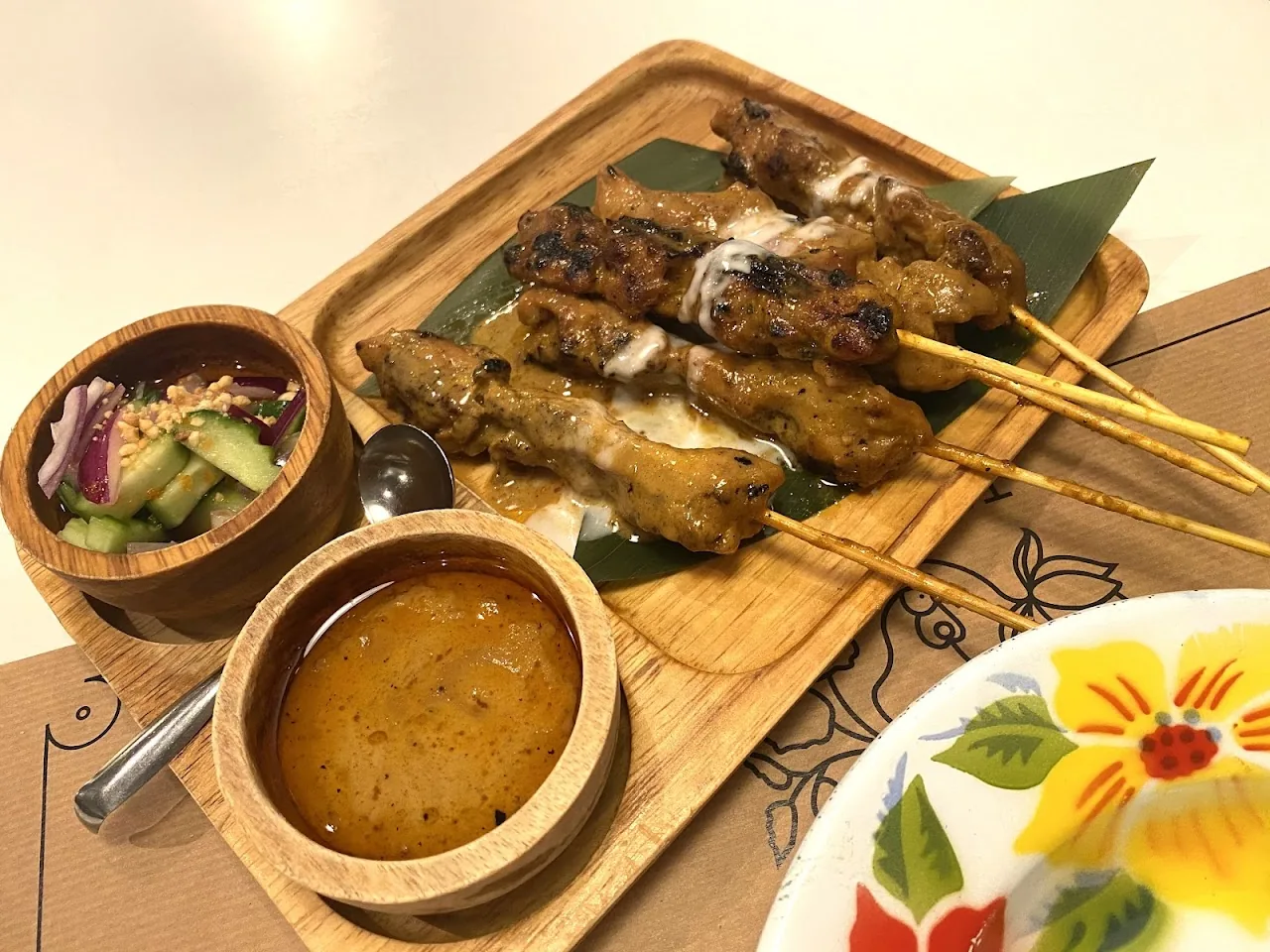 Grilled meat skewers on a wooden board with dipping sauce and a side salad