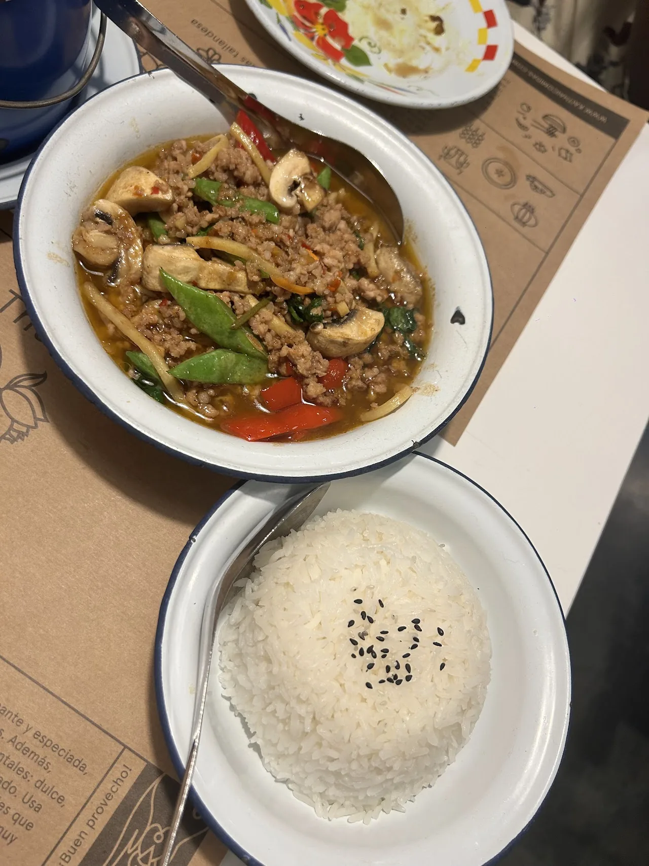 A bowl of Thai soup with mushrooms and herbs beside a bowl of rice