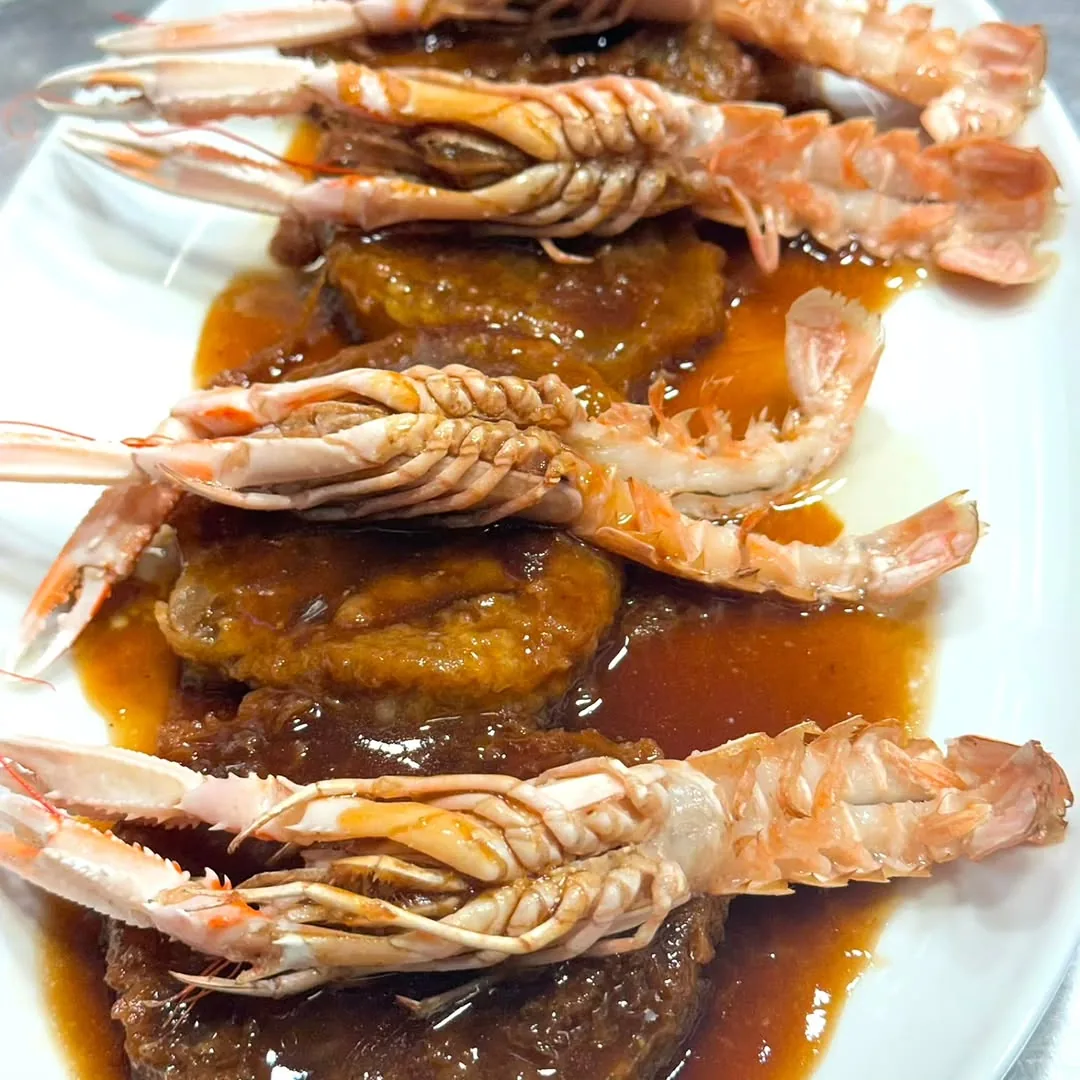 Grilled whole prawns arranged over a bed of sauce and diced mango on a white plate
