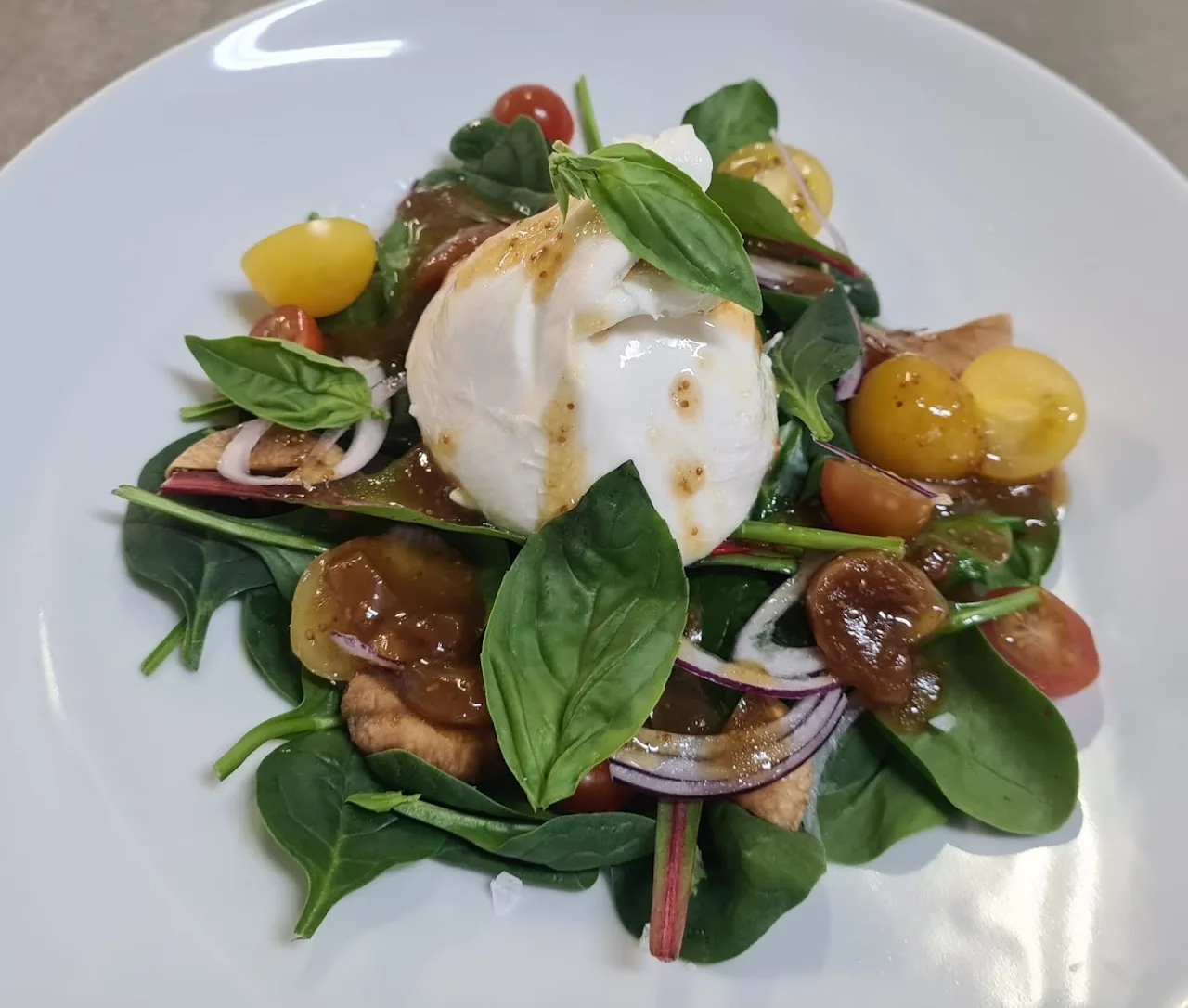 A salad with burrata, cherry tomatoes, spinach, and red onion