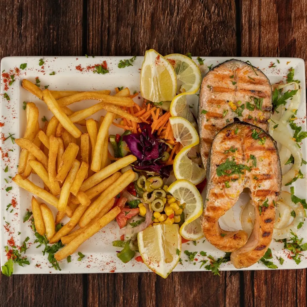 Grilled salmon steaks with fries, lemon wedges, and a mixed vegetable salad on a white plate, at Kapadokya