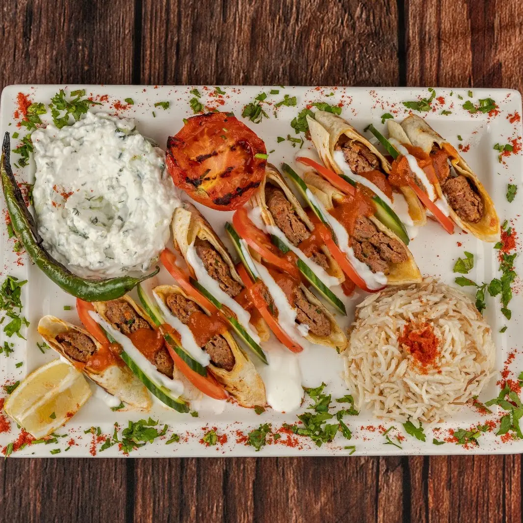 Grilled kofte wraps with tomato and cucumber, tzatziki, grilled tomato, and rice on a white platter, at Kapadokya