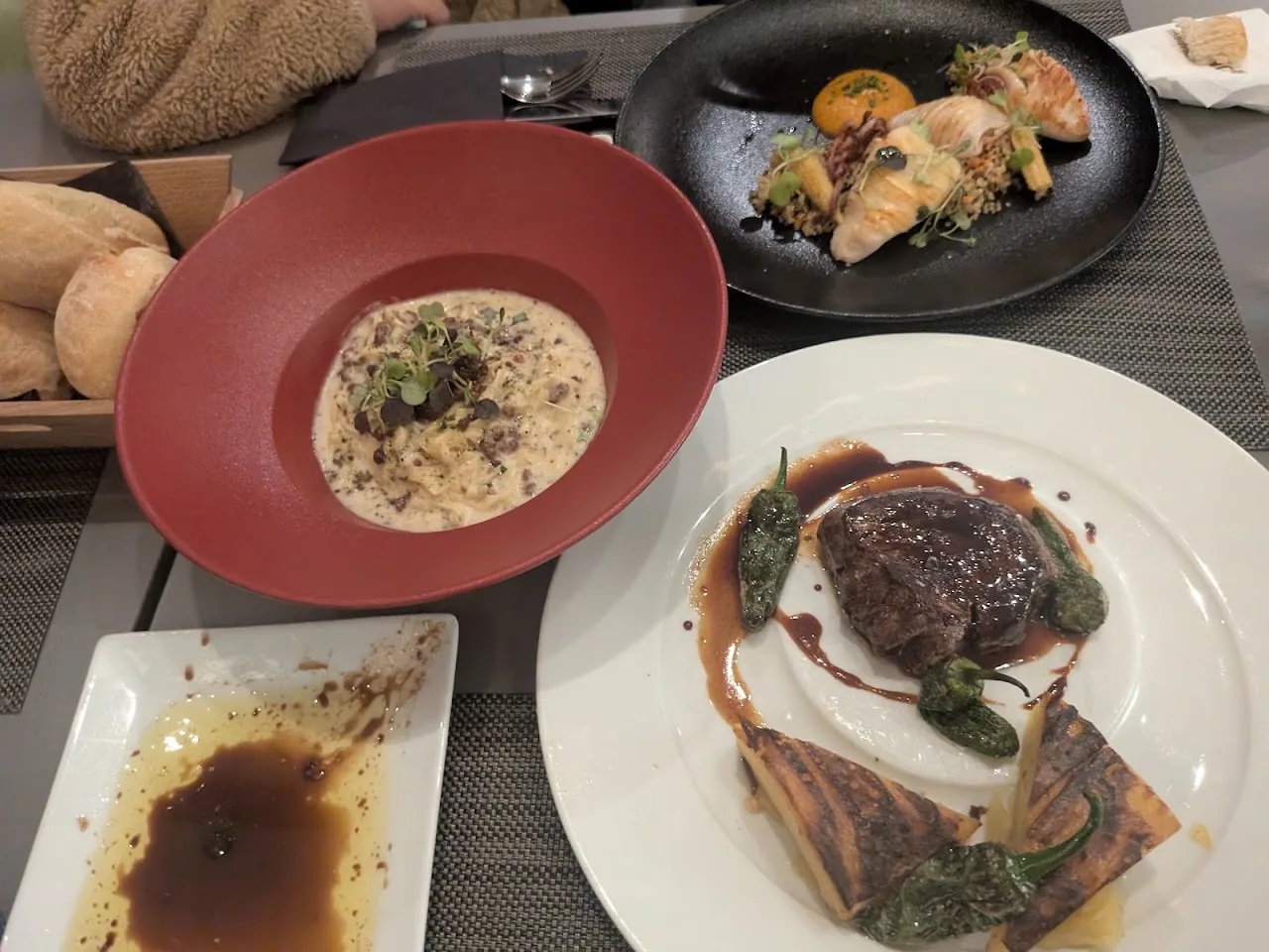 A table spread with a creamy soup, grilled fish, and bread rolls