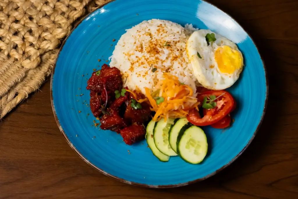 Filipino rice plate on a blue ceramic dish with sweet-and-sour pork, pickled papaya, sliced tomato and cucumber, and a fried egg with runny yolk, Kasarap Filipino Kitchen