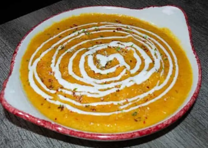 Orange lentil or dal curry with a spiral of cream in a red-rimmed ceramic dish